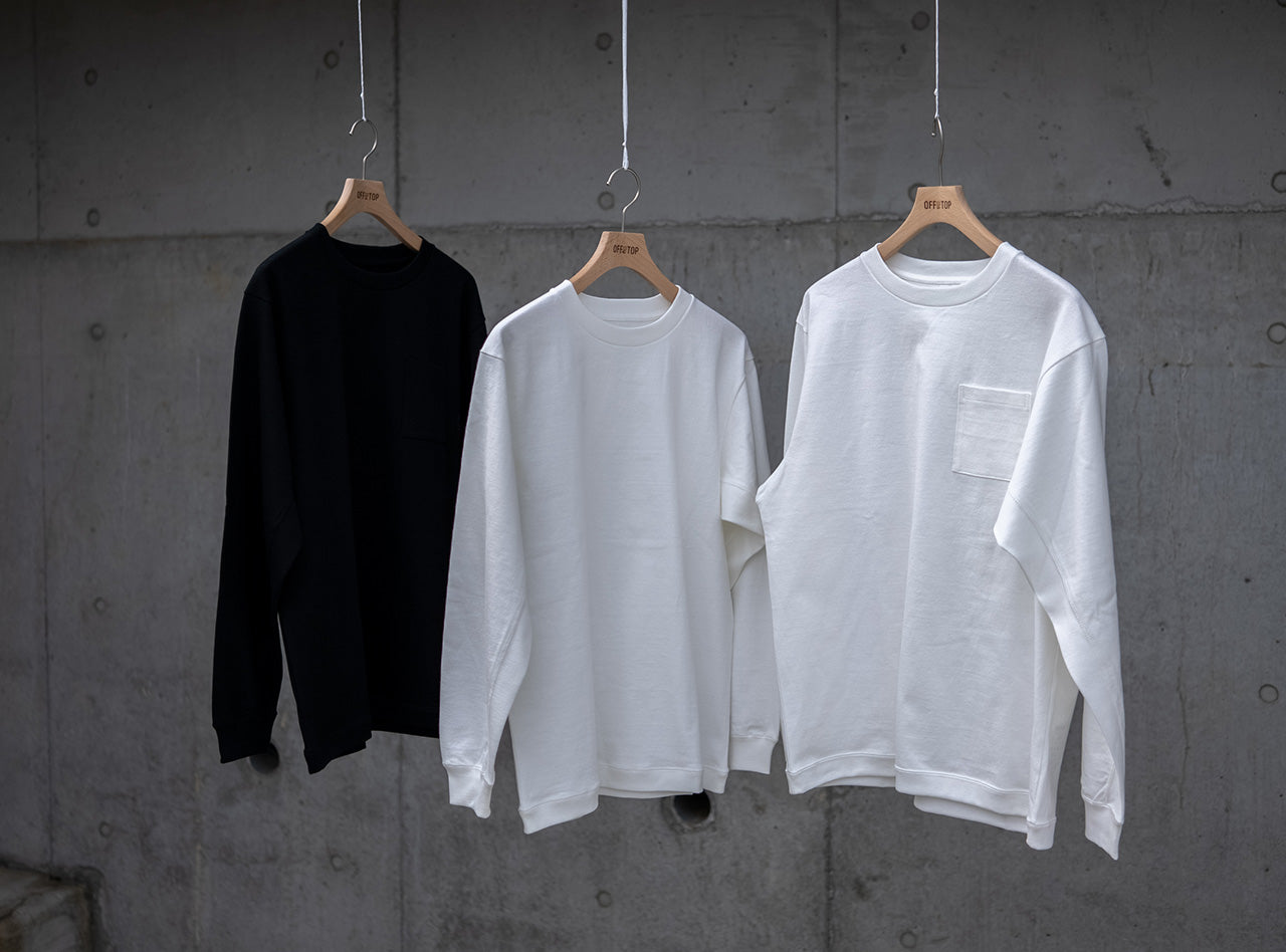 コンクリート壁を背景に吊るされた、10oz（オンス）のヘビーウェイト生地を使用したOFF THE TOPの半袖Tシャツ3型。左からブラック、ホワイト、ホワイト（ポケット付き）。
