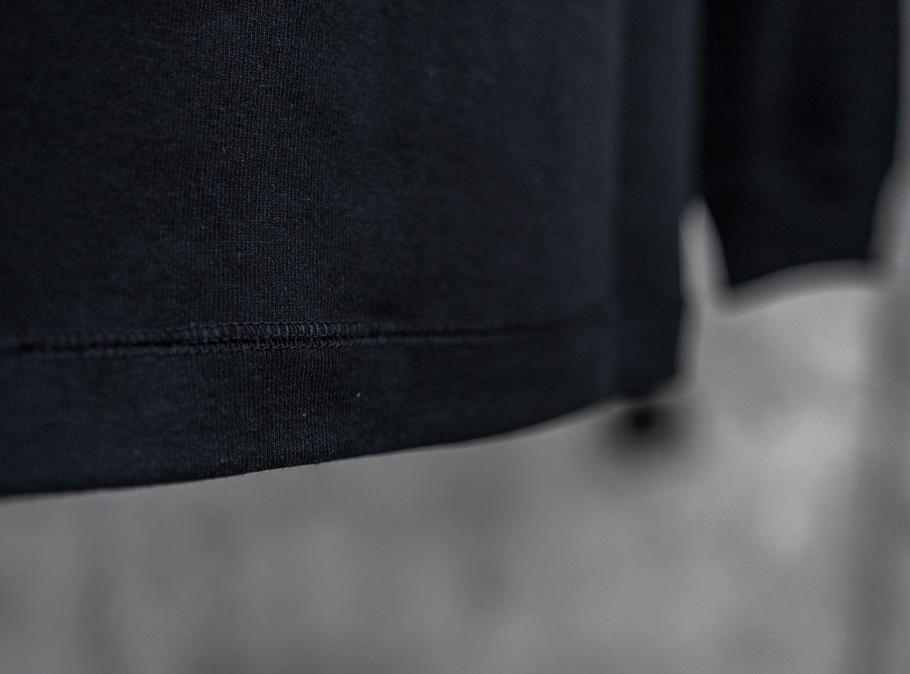 ブラックの新作長袖Tシャツ、裾のクローズアップ。10ozのしっかりとしたヘビーウェイト生地と、耐久性の高いダブルステッチの仕上げ。
