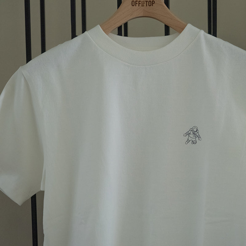 OFF the TOPの木製ハンガーに掛かったホワイトの半袖Tシャツ。左胸部分に、白いラインで描かれた小さな宇宙飛行士のイラストがシルクスクリーンでプリントされています。